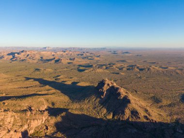 Arizona 'daki Altın Kanyon' daki Batıl inanç Dağları 'nın çöl eteklerindeki hava aracı görüntüsü. Öğleden sonra geç saatlerde güneş ışığı engebeli Sonoran arazisi üzerinde uzun gölgeler ve engin, berrak mavi gökyüzünün altında volkanik tepeler yaratır..