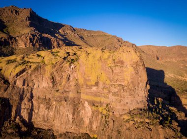 Arizona 'daki Altın Kanyon Superstition Dağları' ndaki devasa volkanik kayaların yakın görüntüsü. Öğleden sonra güneşi, Sonoran Çölü 'ndeki derin mavi gökyüzüne karşı kayalıkların sarı ve engebeli dokusunu vurguluyor..