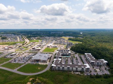 Wendell, Kuzey Carolina 'daki Treelight Meydanı' nın geniş bir insansız hava aracı görüntüsü. Sahne, yüzme havuzları, geniş perakende otoparkları ve parlak bir gökyüzü altında yeni ticari büyüyen modern çoklu aile apartmanlarını ön plana çıkarıyor..