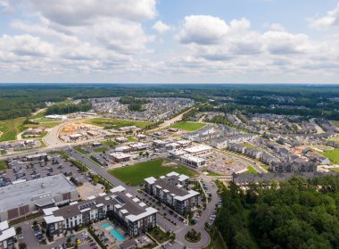 Wendell, Kuzey Carolina 'da büyük planlanmış bir topluluğun geniş bir hava aracı görüntüsü. Çekimler, yemyeşil bir orman ve bulutlu bir ufka karşı kurulmuş manzaralı bir gölün yanında modern tek aile evleri ve kasaba evlerinin sıralarını yakalıyor..