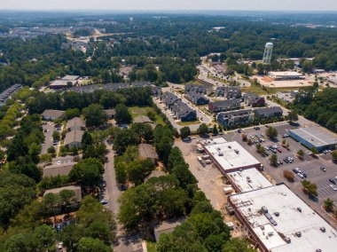 Wake Forest, NC 'deki bir banliyö ticari ve konut koridorunun insansız hava aracı görüntüsü. Görüntü büyük bir perakende binası, geniş otoparklar, modern şehir merkezi kümeleri ve yapraklı ufukta iki farklı beyaz su kulesi yakalıyor..