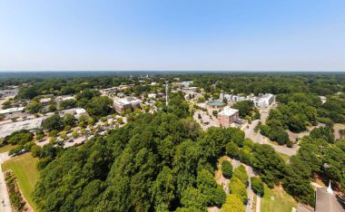 Wake Forest, NC 'a tepeden bakan yüksek irtifalı hava aracı panoraması. Çekim, şehir merkezindeki tarihi binalar, kilise kuleleri ve uzak mesafeden görülen modern yerleşim yerleriyle ön planda büyük bir yeşil ağaç gölgesini yakalıyor..