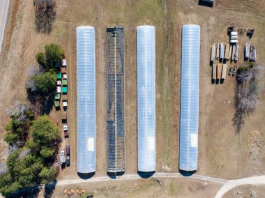Çiftlikteki endüstriyel seraların yukarıdan aşağıya bakış açısı. Çekimde üç plastik kaplı yapı ve bir açık çerçeve, depolama alanları, araçlar ve hasat edilen kereste, tarımsal altyapı ve ölçeklendirmenin yanı sıra.