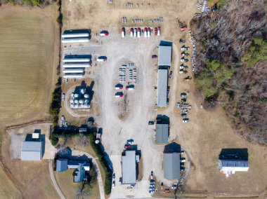 Propan gazı dağıtım merkezinin geniş çaplı tepeden tırnağa drone görüntüsü. Manzarada büyük depolama tankları, nakliye kamyonları, erzak depoları ve çakıl taşı parkında sıralanmış silindirler var..