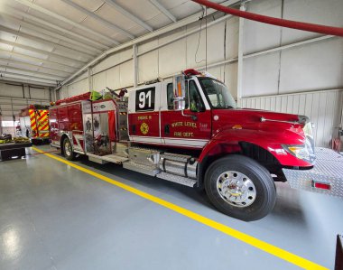 91. Şube 'nin yan görüntüsü. Beyaz Seviye İtfaiye' den kırmızı beyaz bir itfaiye aracı. Araç gri bir epoksi zeminde park halinde, üzerinde altın harfler, krom tekerlekler ve takside açıkça 