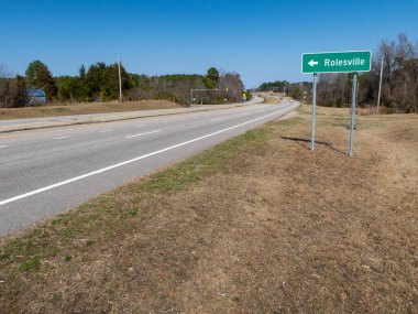 Kuzey Carolina Rolesville 'e doğru giden yeşil bir otoyol işaretinin zemin katındaki görüntüsü. İşaret, çok şeritli bölünmüş bir otoyol boyunca, açık mavi bir gökyüzünün altında, uzaktaki ışık trafiğinin görülebildiği metal direklerde duruyor..