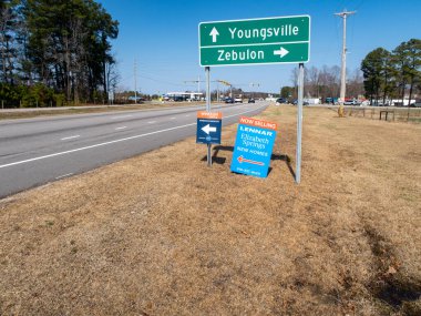 Youngsville ve Zebulon, NC için yol tabelalarının zemin katındaki manzaraya Winston Ridge ve Elizabeth Springs için emlak tabelaları eşlik ediyor. İşaretler Kuzey Carolina 'da açık bir gökyüzünün altında çok şeritli bir yol boyunca yer alıyor..