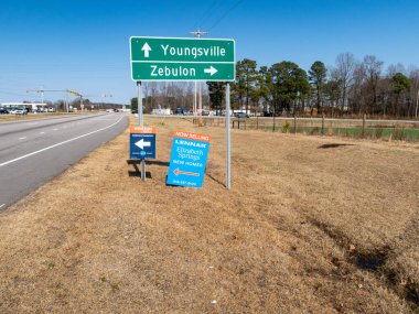 Youngsville ve Zebulon, NC için yol tabelalarının zemin katındaki manzaraya Winston Ridge ve Elizabeth Springs için emlak tabelaları eşlik ediyor. İşaretler Kuzey Carolina 'da açık bir gökyüzünün altında çok şeritli bir yol boyunca yer alıyor..