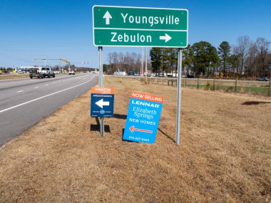 Youngsville ve Zebulon, NC için yol tabelalarının zemin katındaki manzaraya Winston Ridge ve Elizabeth Springs için emlak tabelaları eşlik ediyor. İşaretler Kuzey Carolina 'da açık bir gökyüzünün altında çok şeritli bir yol boyunca yer alıyor..
