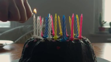 Evde doğal pencere ışığıyla aile kutlaması. Çikolatalı kekin üzerine mum koyan bir anne ve çocuğun yakın plan görüntüleri. Yüksek kalite 4k görüntü