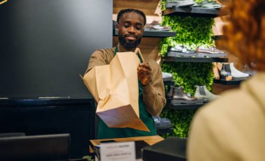 Mağazada genç beyaz bir adam alışveriş poşetini genç kadınlara veriyor. Yüksek kalite fotoğraf Genç Kafkasyalı bir dükkanda alışveriş çantası teslim eden genç bir adam