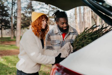 Genç çift arabada Noel ağacı paketliyor. Kaliteli fotoğraf. Genç çift arabada Noel ağacı paketliyor.
