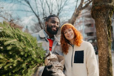 Yaklaşan tatiller için aldıkları Noel ağacını taşıyan mutlu bir çift. Yüksek kalite fotoğraf çeken mutlu bir çift Noel ağacı taşıyor ve gelecek tatiller için satın alıyorlar.