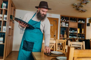 Gülümseyen garson masaları temizleyip düzenliyor. Yüksek kalite fotoğraf çeken, gülümseyen garson masaları temizleyip düzenliyor.