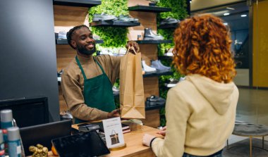 Mağazada genç beyaz bir adam alışveriş poşetini genç kadınlara veriyor. Yüksek kalite fotoğraf Genç Kafkasyalı bir dükkanda alışveriş çantası teslim eden genç bir adam
