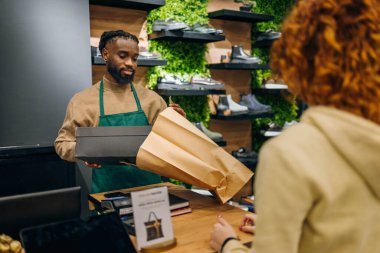 Mağazada genç beyaz bir adam alışveriş poşetini genç kadınlara veriyor. Yüksek kalite fotoğraf Genç Kafkasyalı bir dükkanda alışveriş çantası teslim eden genç bir adam