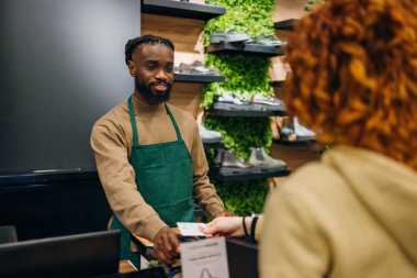 Mağazada genç beyaz bir adam alışveriş poşetini genç kadınlara veriyor. Yüksek kalite fotoğraf Genç Kafkasyalı bir dükkanda alışveriş çantası teslim eden genç bir adam