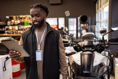 Elinde tablet tutan motosiklet malzemeleri satıcısı. Motosiklet malzemeleri satıcısı elinde tablet tutuyor.