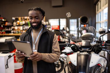 Elinde tablet tutan motosiklet malzemeleri satıcısı. Motosiklet malzemeleri satıcısı elinde tablet tutuyor.