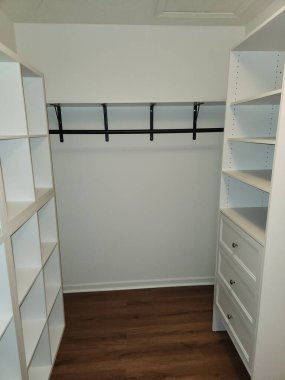 Modern gömme dolap. Rafları, çekmeceleri ve asma çubuğu var. Temiz beyaz dolap ve ahşap döşeme ev organizasyonu, iç tasarım ve emlak kavramları için minimalist, düzenli bir alan yaratıyor..