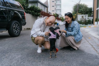 Dışarıda çömelmiş ve evcil köpekleriyle etkileşim halinde olan iki neşeli kadın.