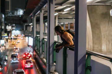 Yükseltilmiş bir geçitten gece manzarasını çeken kameralı bir fotoğrafçı.