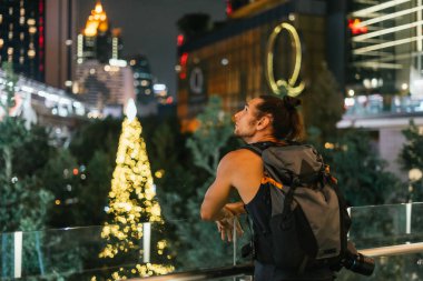 Sırt çantalı adam şehrin ışıklarına ve şenlikli dekorasyonlarına hayran.