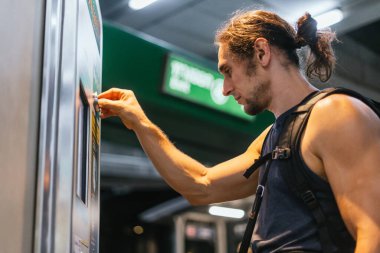 Toplu taşıma istasyonunda bilet otomatı kullanan bir adam.