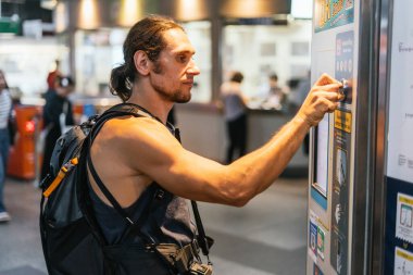 Tren istasyonunda otomatik otomat kullanan sırt çantalı bir adam.