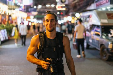 Sırt çantası takan ve kalabalık bir caddede elinde kamera olan genç bir adam.