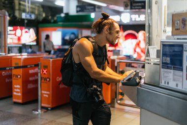 Sırt çantalı ve kameralı bir adam terminalden bilet alıyor.