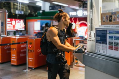 Sırt çantalı ve kameralı bir turist şehir taşıma istasyonundan bilet alıyor.