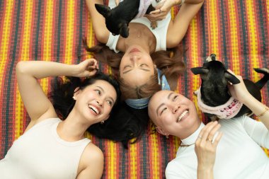 Çizgili bir hasırda evcil köpeklerle rahatlarken gülümseyen çeşitli kadınlar.