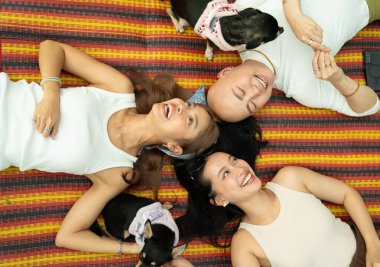 Gülümseyen arkadaşlar ve renkli bir mindere uzanmış iki köpek birlikte vakit geçirmenin tadını çıkarıyorlar.