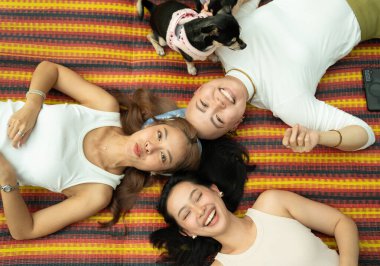 Üç yetişkin kadın ve bir chihuahua köpeği mindere uzanmış gülümsüyor ve yukarı bakıyor.