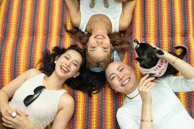 Üç gülümseyen genç kadın ve çizgili bir paspasın üzerinde rahatlayan küçük bir köpek.