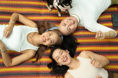 Mutlu kadınlar ve küçük bir köpek bir paspasın üzerinde dinleniyorlar, yukarıdan kameraya gülümsüyorlar.