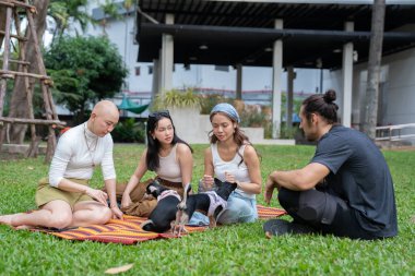 Bir grup arkadaş ve köpekleri parkta bir piknik minderinde eğleniyorlar.