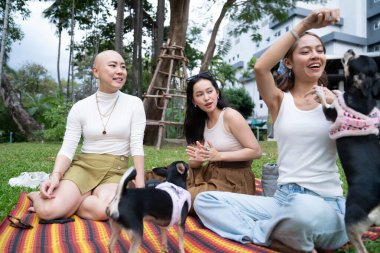 Bayan arkadaşlar evcil köpekleriyle parkta piknik yapıyorlar.