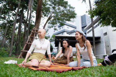 Kadın arkadaşlar parkta piknik yaparken çimlerin üzerinde oturur, konuşur ve dinlenirler.
