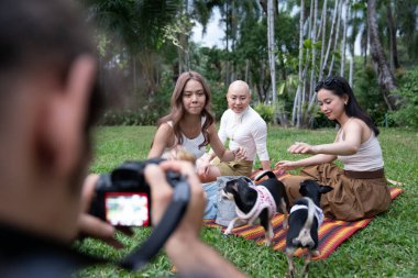 Arkadaşlar ve köpekler fotoğraf çekilirken parkta piknik yapıyorlar.