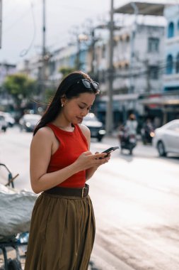 Şehirdeki bir caddede cep telefonuna dalmış Asyalı genç bir kadın.