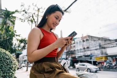 Dışarıdaki cep telefonuna bakan genç bir kadın, şehir çevresi ile çevrili.