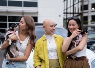 Üç farklı kadın arkadaş küçük köpekleri ile neşeli bir şekilde dışarıda vakit geçiriyorlar.