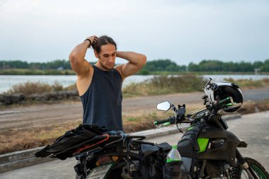 Tam teçhizatlı bir motosikletin yanında duran adam saçlarını düzeltiyor.