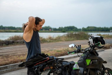 Bir adam açık yolda motosiklet sürmeden önce geriniyor.