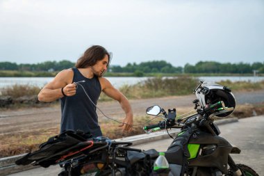 Şarj kablosu tutan bir adam, motorsikletle seyahat ederken cihazlarına güç vermeye hazırlanıyor.