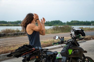 Uzun saçlı bir adam motosiklet yolculuğu için kask takıyor.