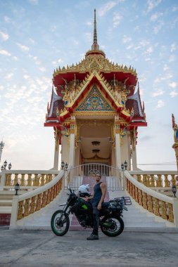 Tayland 'da geleneksel bir Tayland tapınağında motosikletin yanında duran genç adam.