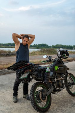 Macera motosikletinin yanında duran adam, uzun bir yolculuk için teçhizat takıyor.